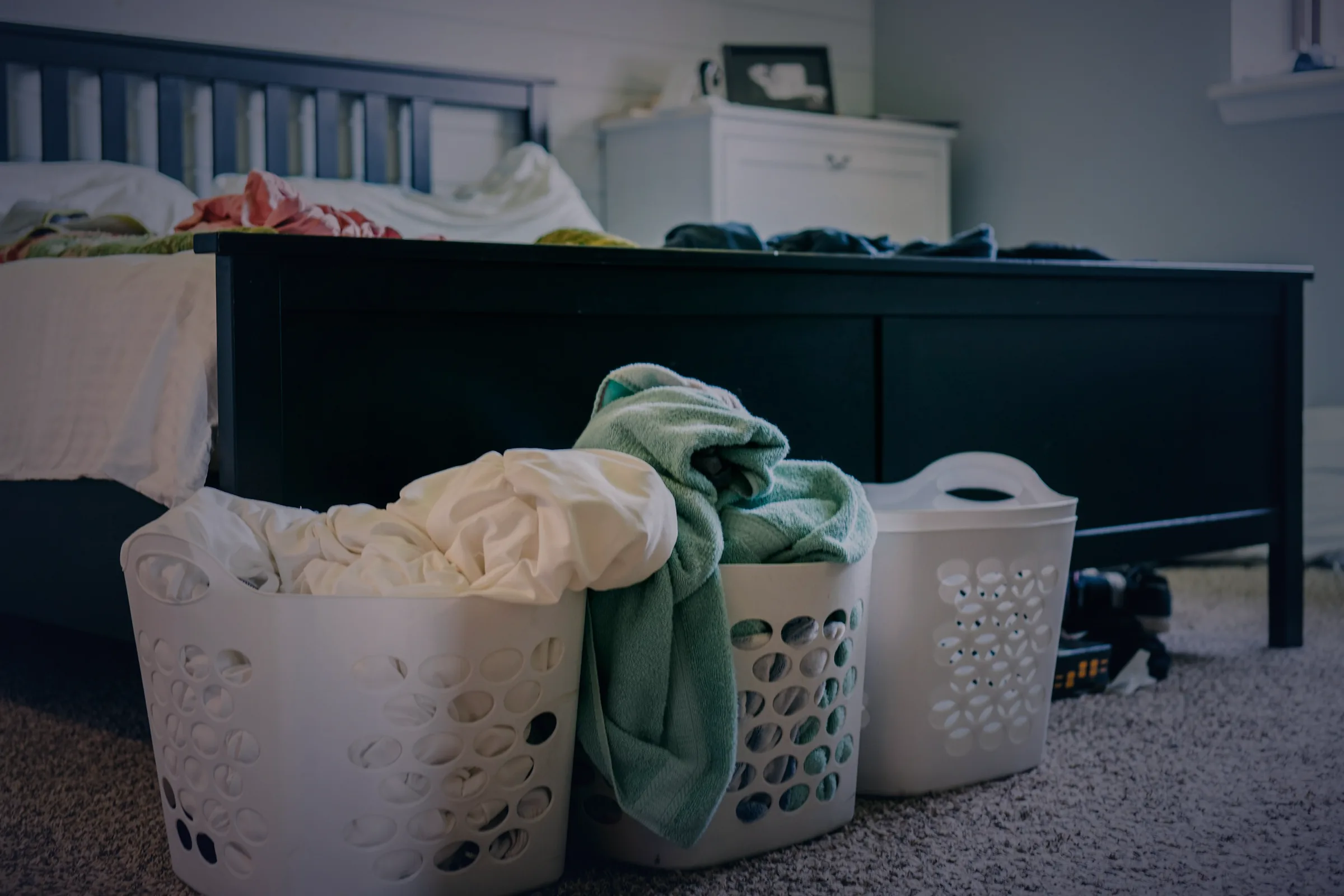Laundry baskets overflowing at the foot of a bed
